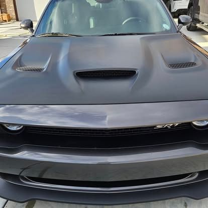 Close-up front view of a dark gray Dodge Challenger SRT with a matte black vented hood, parked on a paved driveway.