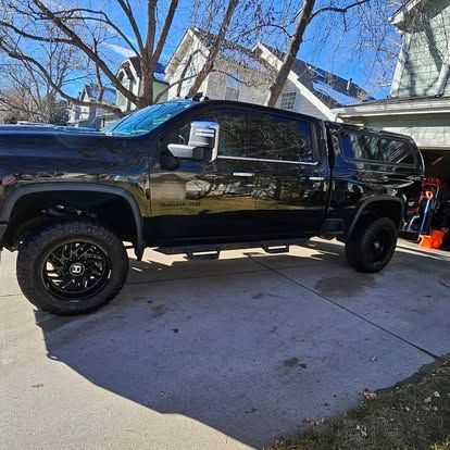 A black pickup truck with a camper shell parked on a residential driveway on a sunny day.
