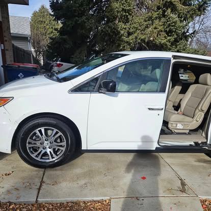 A white minivan parked on a driveway with its side sliding door open, revealing the tan interior seats.