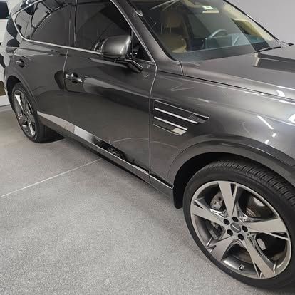 A dark gray Genesis GV80 SUV parked on a concrete floor, viewed from the front passenger side.