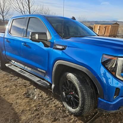 A bright blue GMC Sierra pickup truck parked on a dirt lot with a wooden shed in the background.
