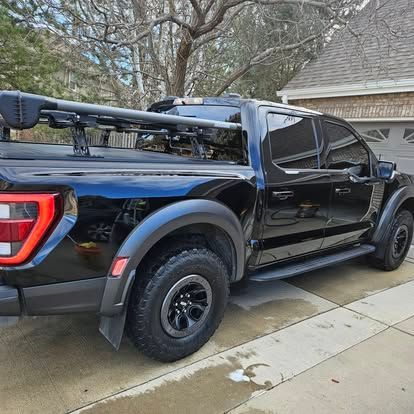 A black Ford F-150 truck with a roof rack parked in a residential driveway on a cloudy day.