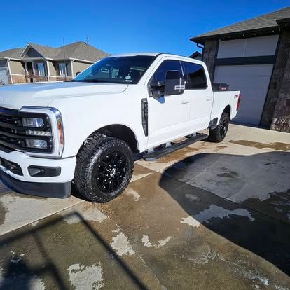 A white Ford Super Duty pickup truck with black wheels parked in a concrete driveway in front of a residential garage.