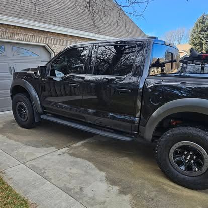 A black Ford F-150 Raptor pickup truck parked on a concrete driveway in front of a suburban garage.