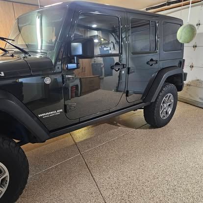 A black four-door Jeep Wrangler parked in a garage with speckled flooring.