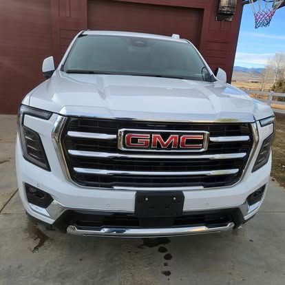 Front view of a white GMC Yukon parked on a concrete driveway in front of a reddish-brown building.