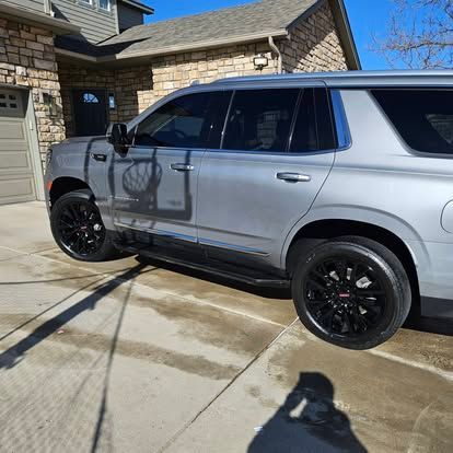 A silver SUV with black rims parked on a concrete driveway in front of a stone house on a sunny day.