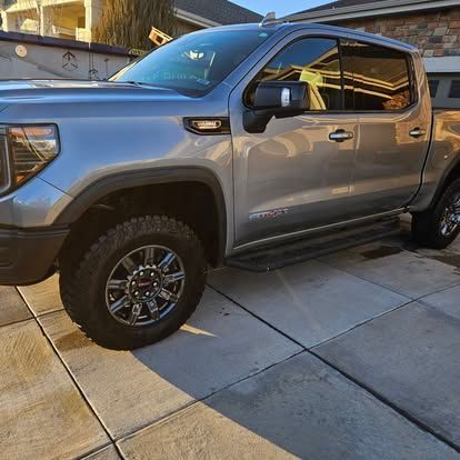 A silver GMC Sierra pickup truck parked on a concrete driveway in front of a house.