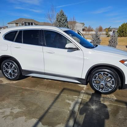 A white BMW SUV parked on a concrete driveway during a sunny day.