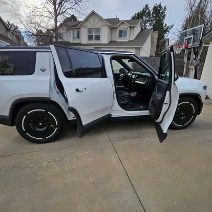 A white SUV parked in a driveway with its front and back passenger doors open, revealing a dark interior.