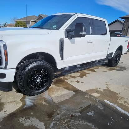 A white Ford F-Series crew cab pickup truck parked on a concrete driveway against a clear blue sky.