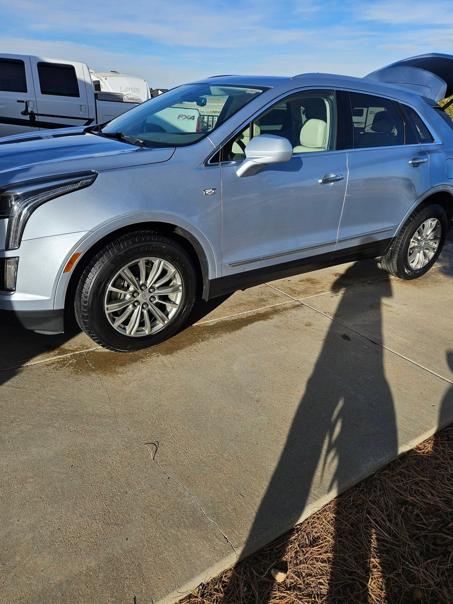A silver Cadillac XT5 parked on a paved lot on a sunny day.