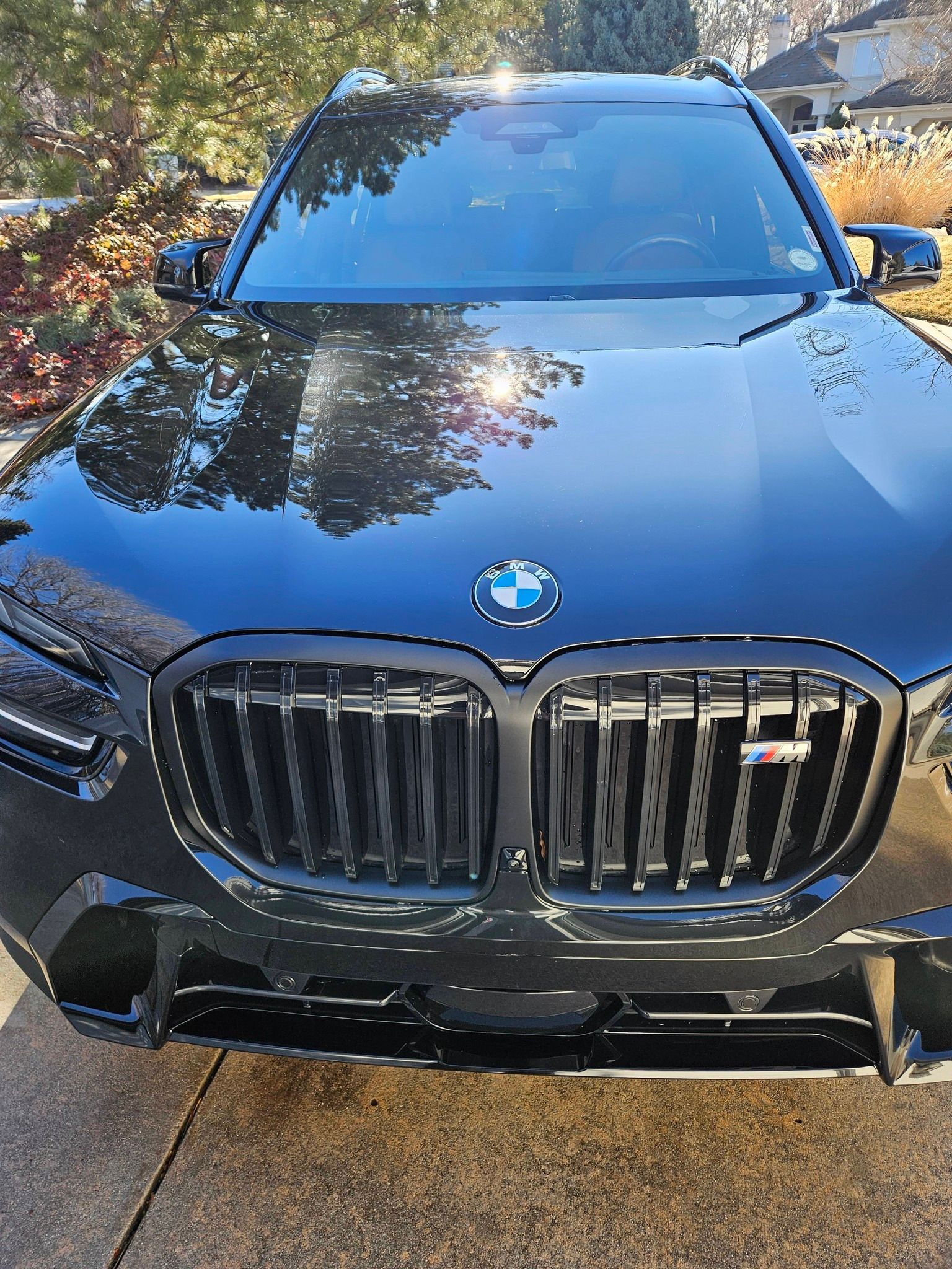 A front-facing view of a shiny, black BMW SUV parked outdoors on a paved surface.