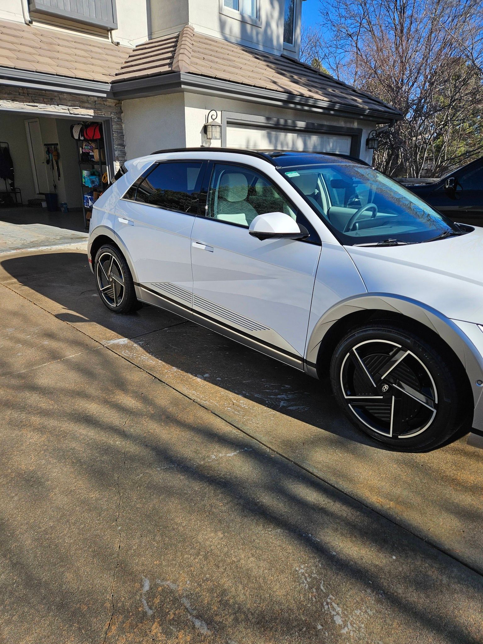 A white Hyundai Ioniq 5 parked on a residential driveway in front of a house on a sunny day.