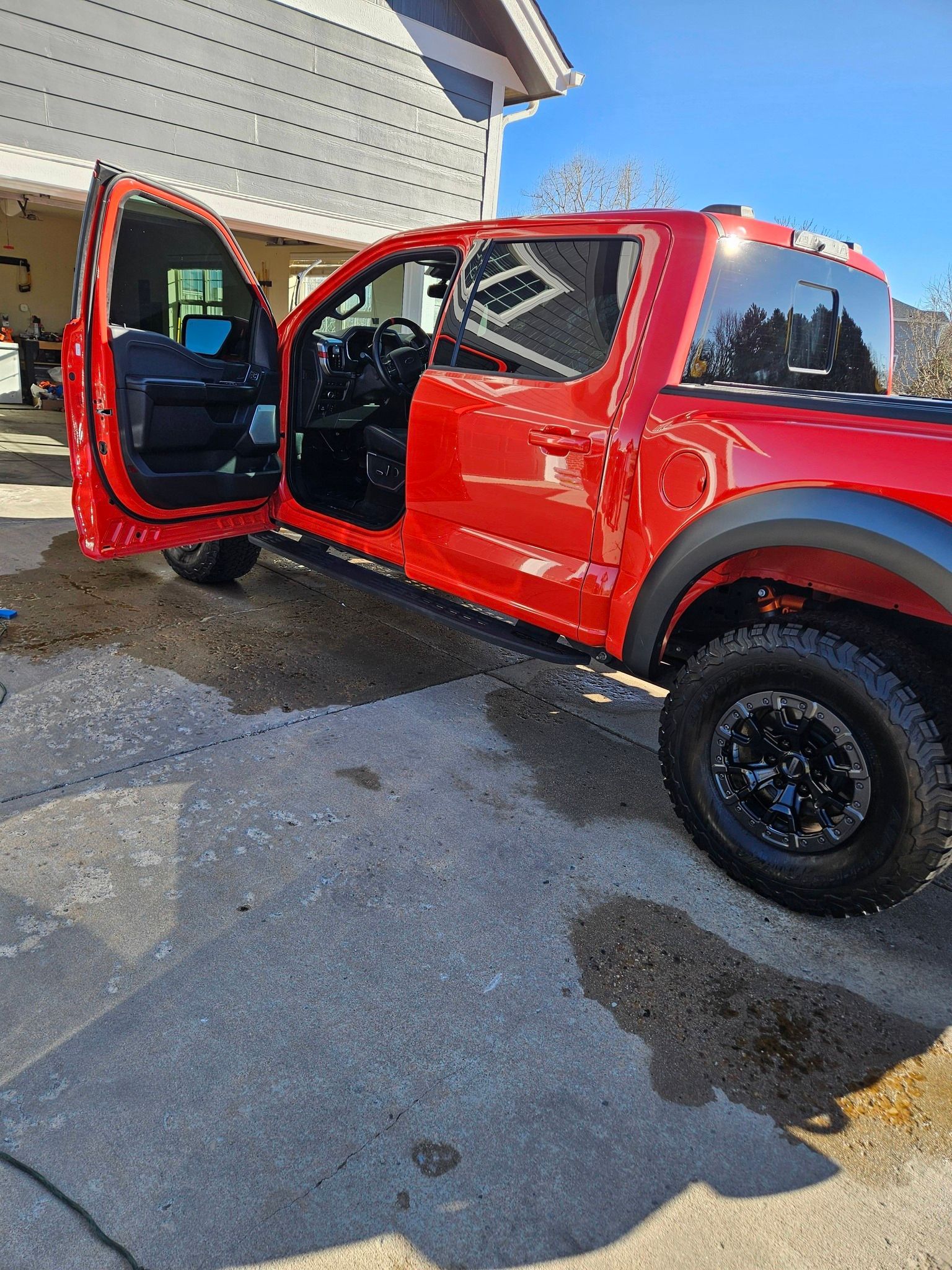 A bright red pickup truck parked on a concrete driveway with its driver-side door open.