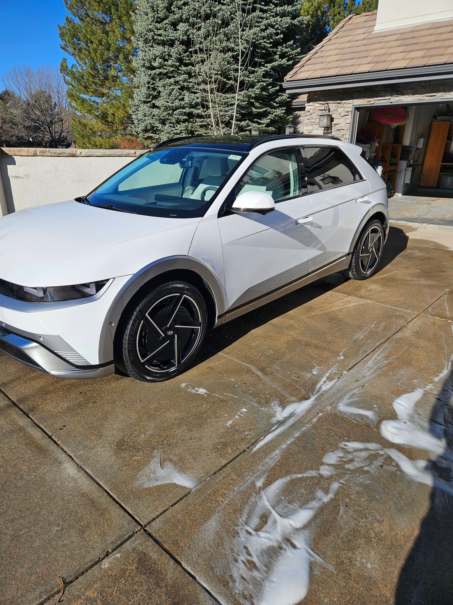 A clean white Hyundai Ioniq 5 parked on a residential driveway, with soap suds visible on the ground after a wash.