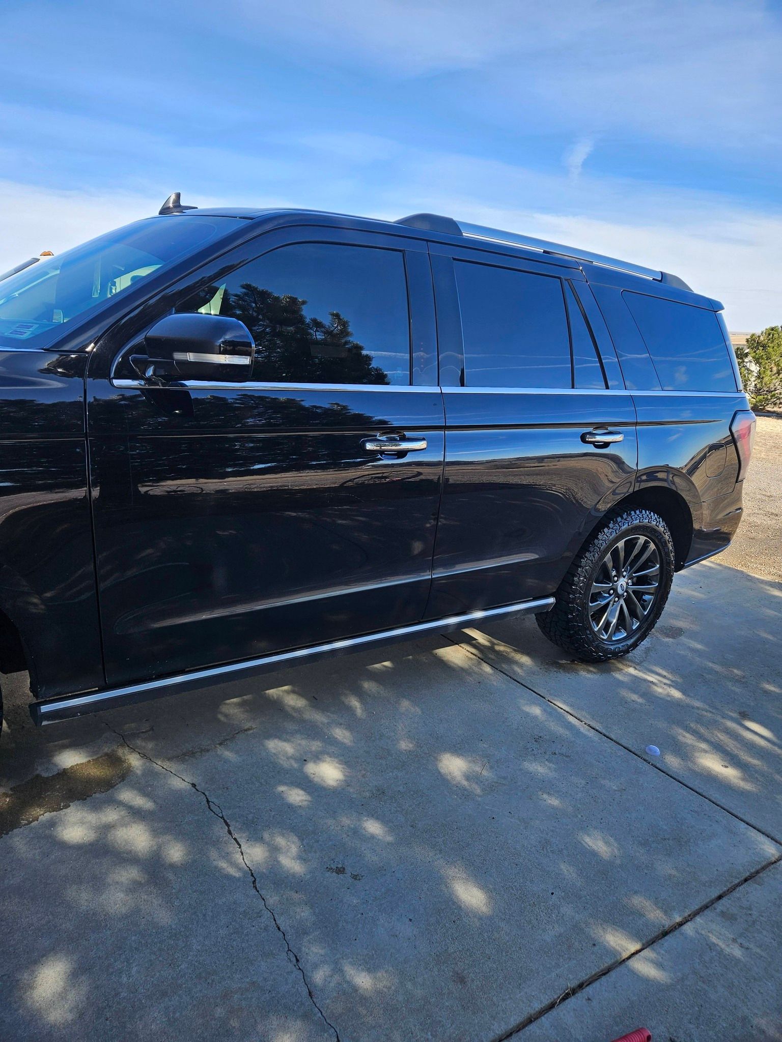 A black Ford Expedition SUV parked on a concrete driveway under a bright blue sky.