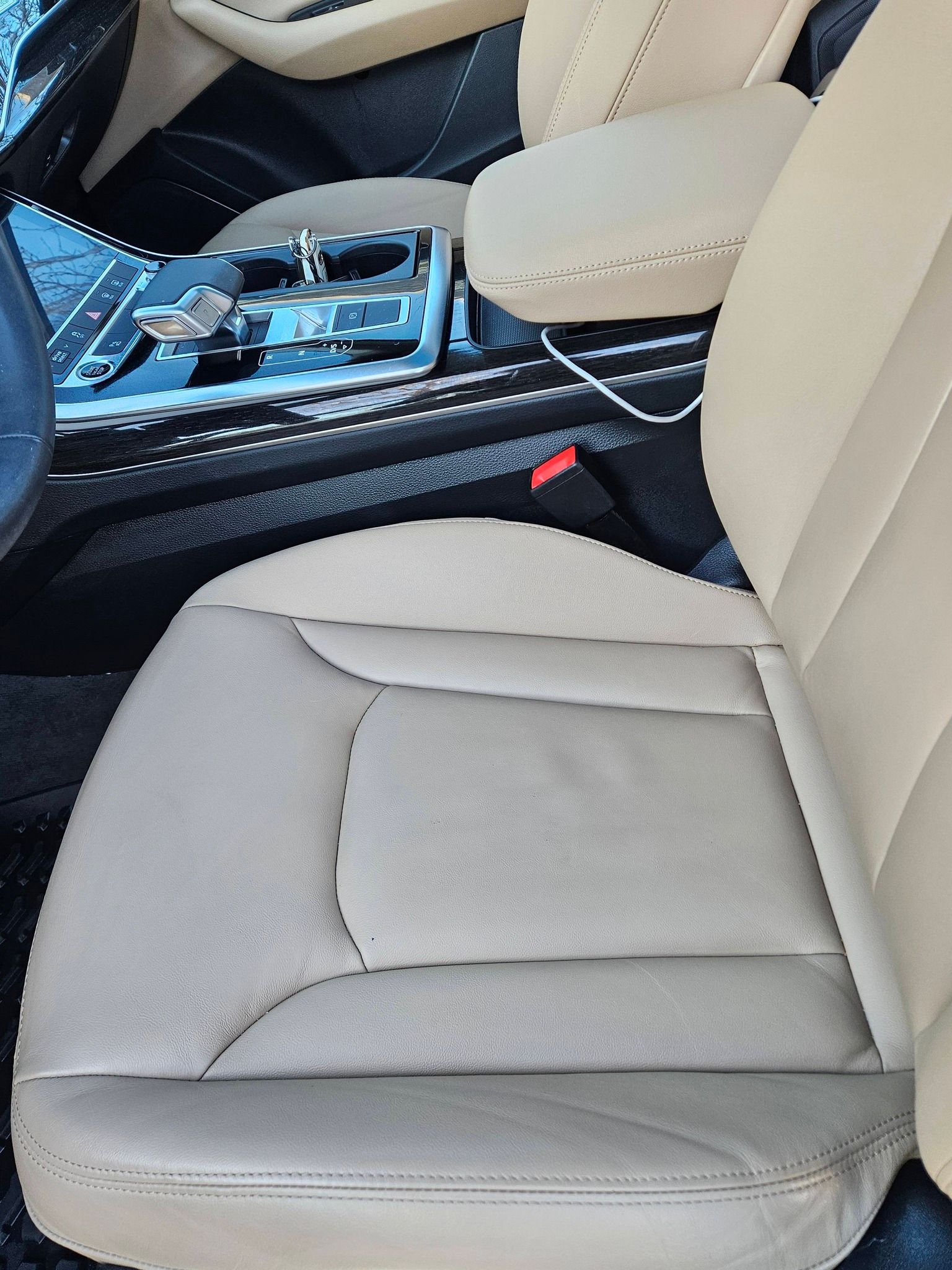 Beige leather car seat interior, featuring a center console with cup holders and a charging cable.