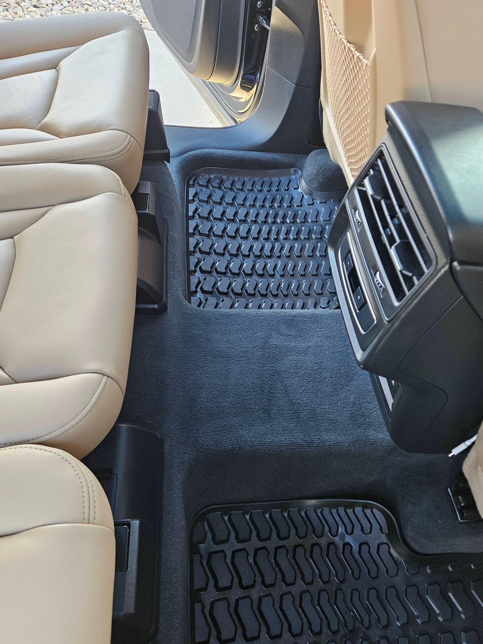 Interior of a vehicle featuring beige leather seats, dark grey carpet, and black rubber floor mats.