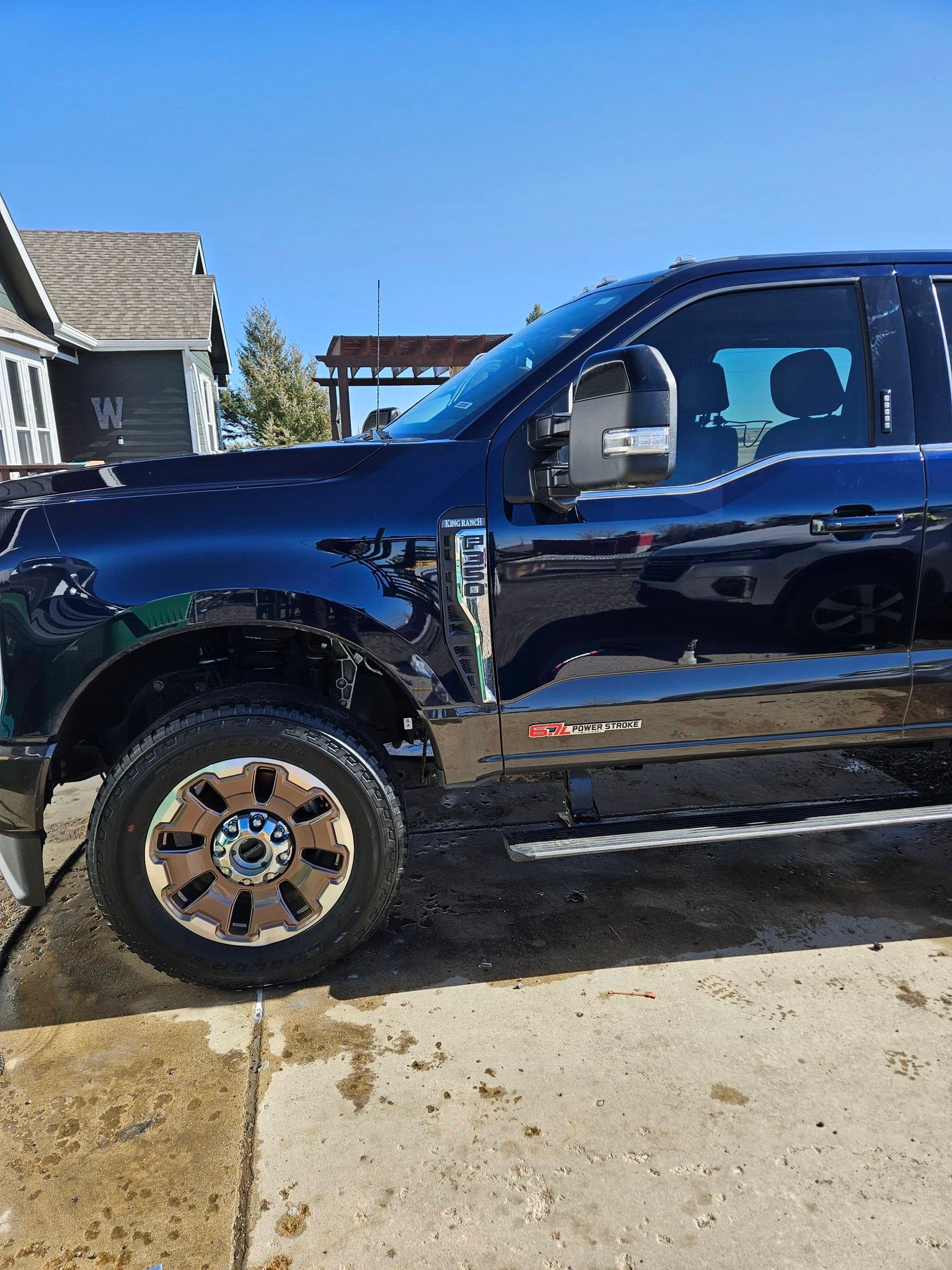 A dark-colored Ford Super Duty pickup truck parked on a concrete driveway during the day.