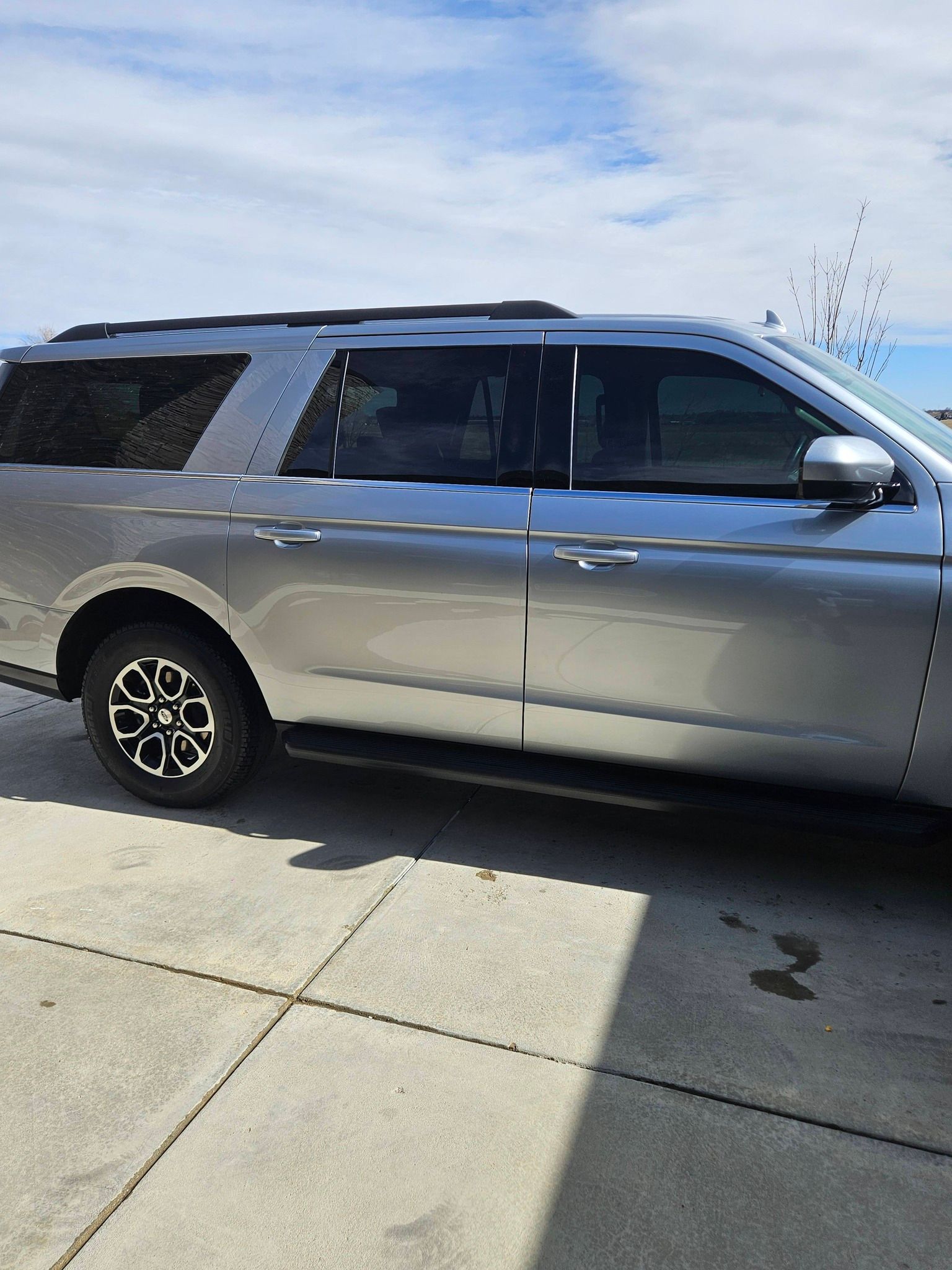 A silver SUV parked on a concrete driveway under a blue, cloudy sky.