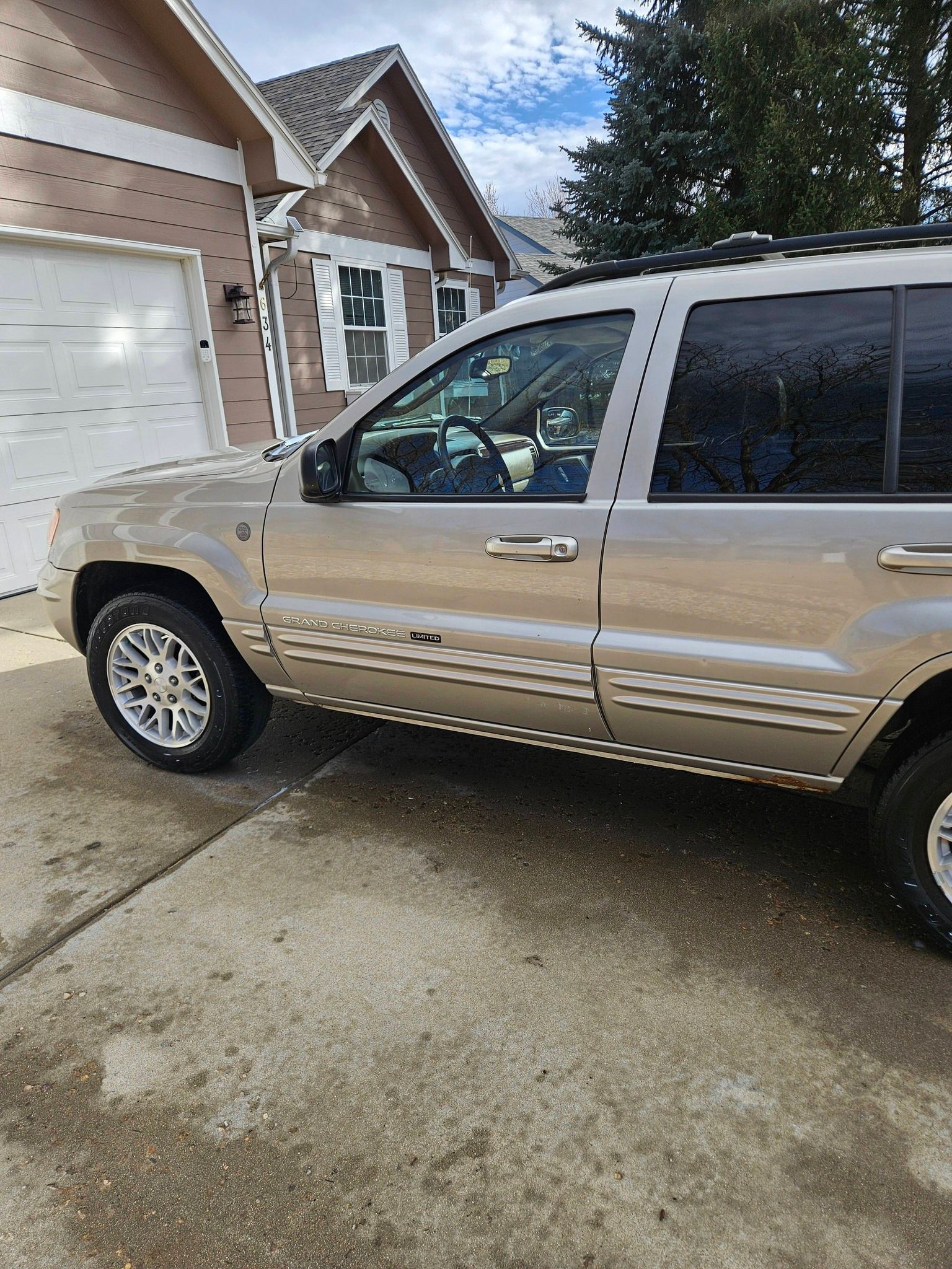 A tan SUV parked in a driveway in front of a house with light brown siding and a closed garage door.