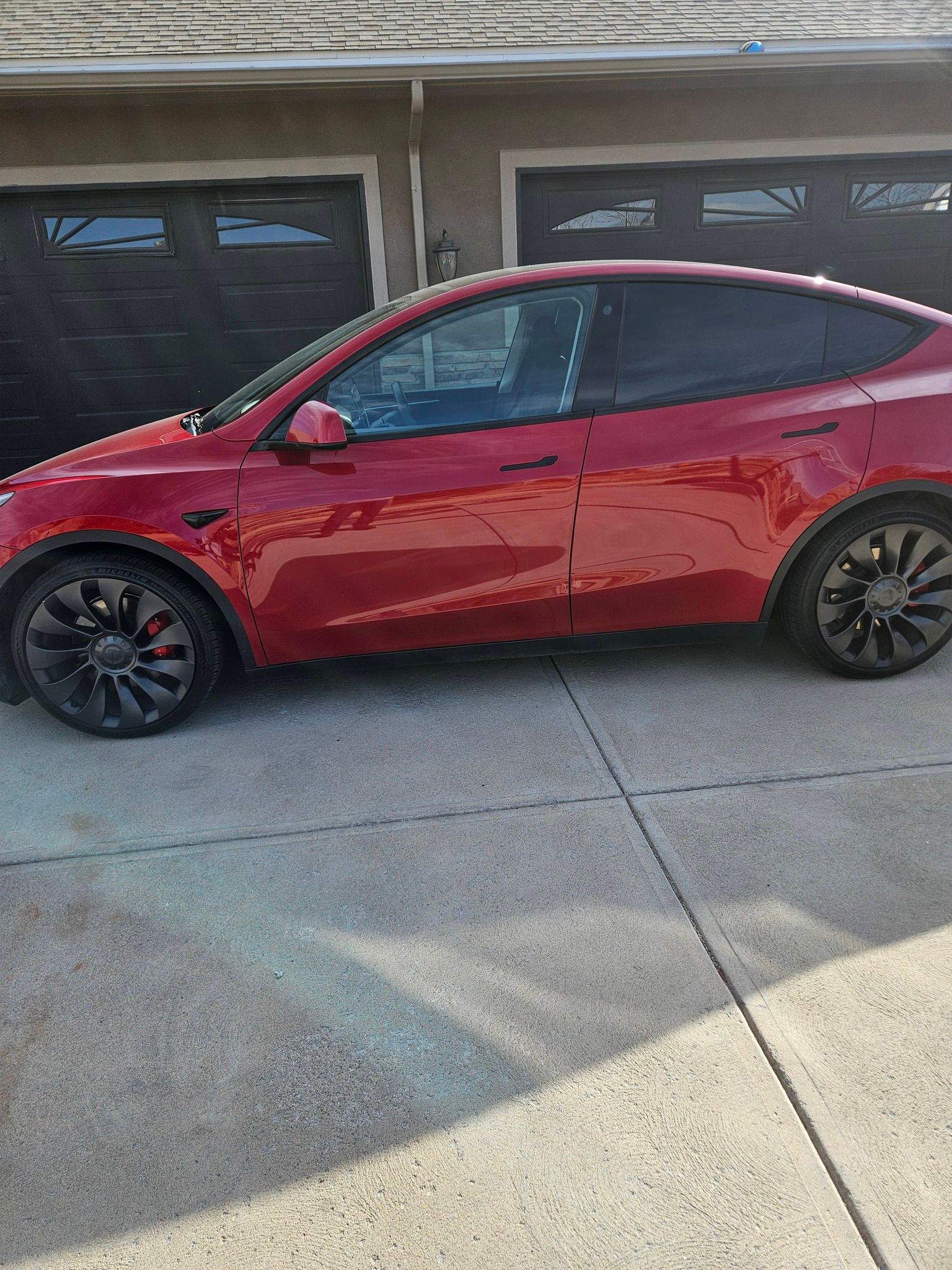 A red Tesla Model Y parked in a residential driveway in front of a multi-car garage.