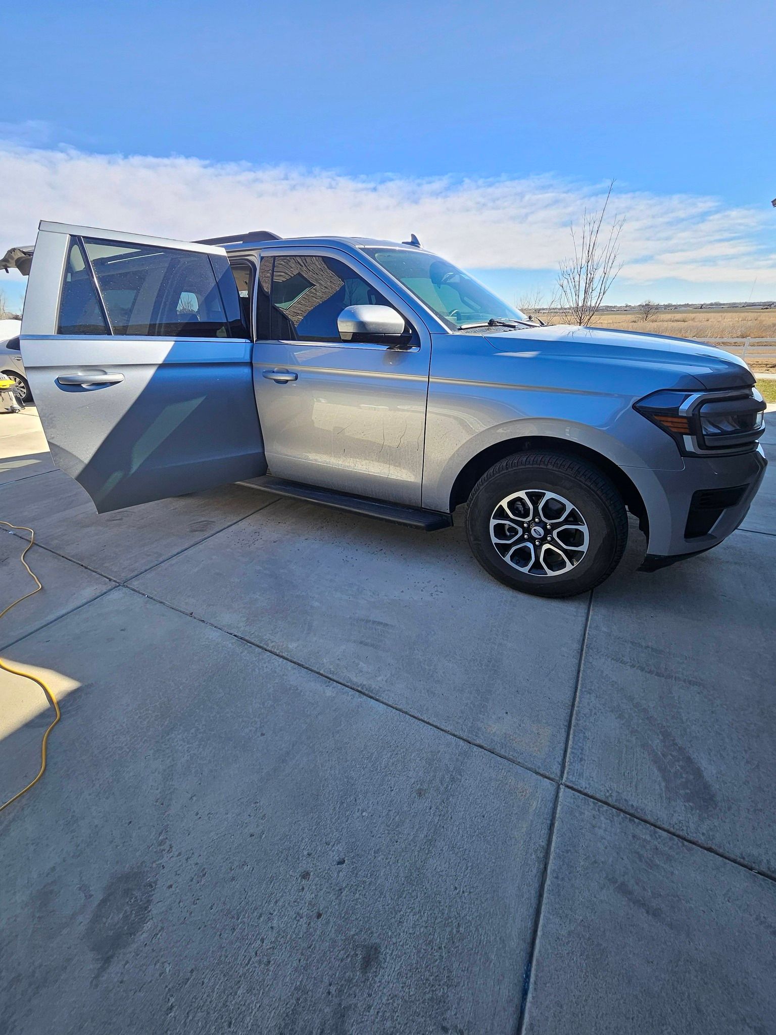 A silver SUV parked on a concrete driveway with its front passenger door open on a sunny day.