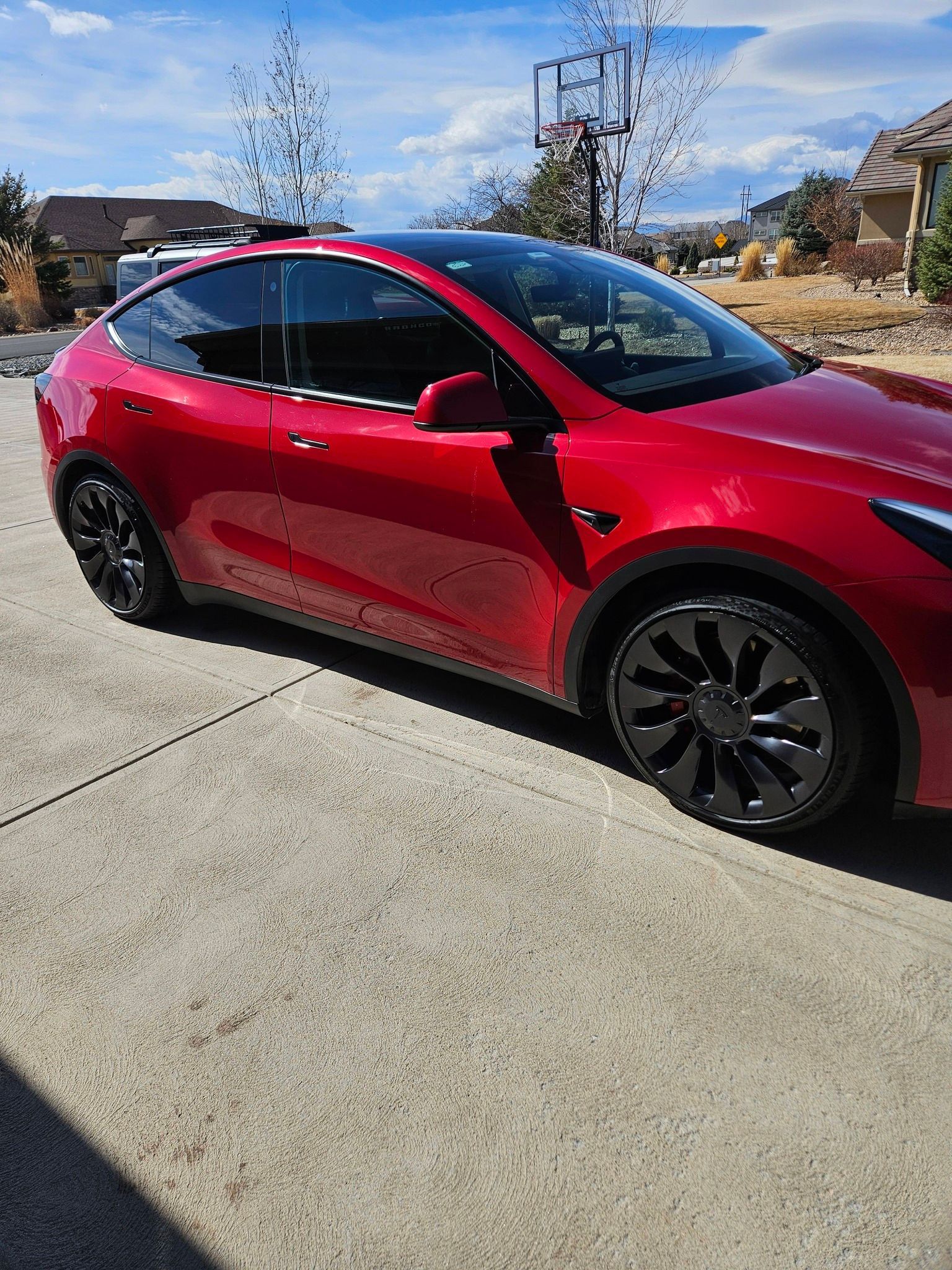 A bright red Tesla Model Y parked on a concrete driveway with large black multi-spoke wheels.