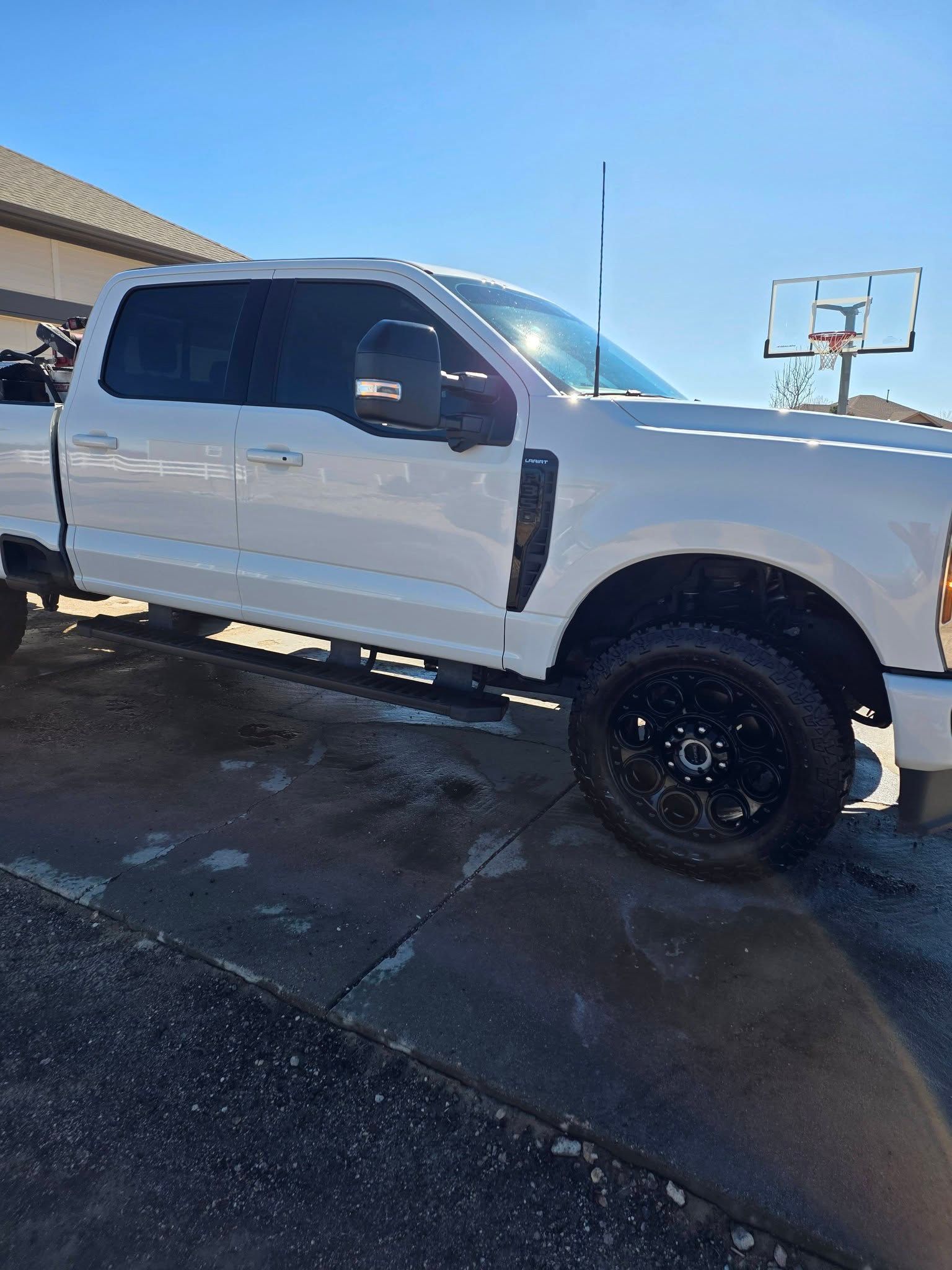 White Ford Super Duty pickup truck parked on a paved driveway with a basketball hoop in the background.