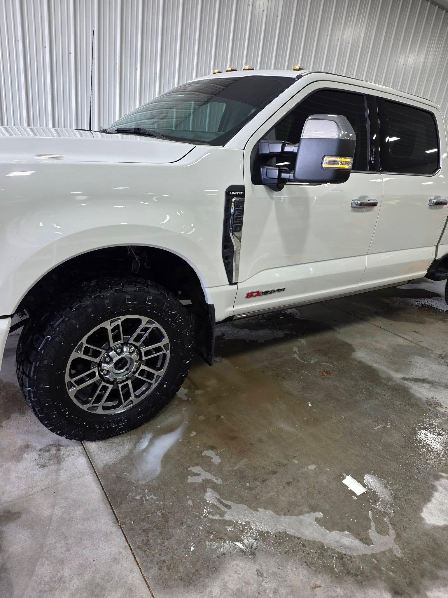 A white Ford Super Duty truck parked inside a garage on a wet concrete floor.