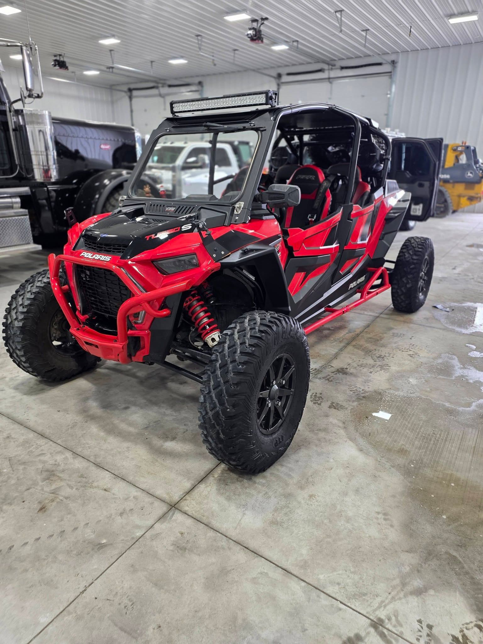 A bright red Polaris RZR off-road vehicle with large black tires, parked inside a spacious, well-lit indoor warehouse.