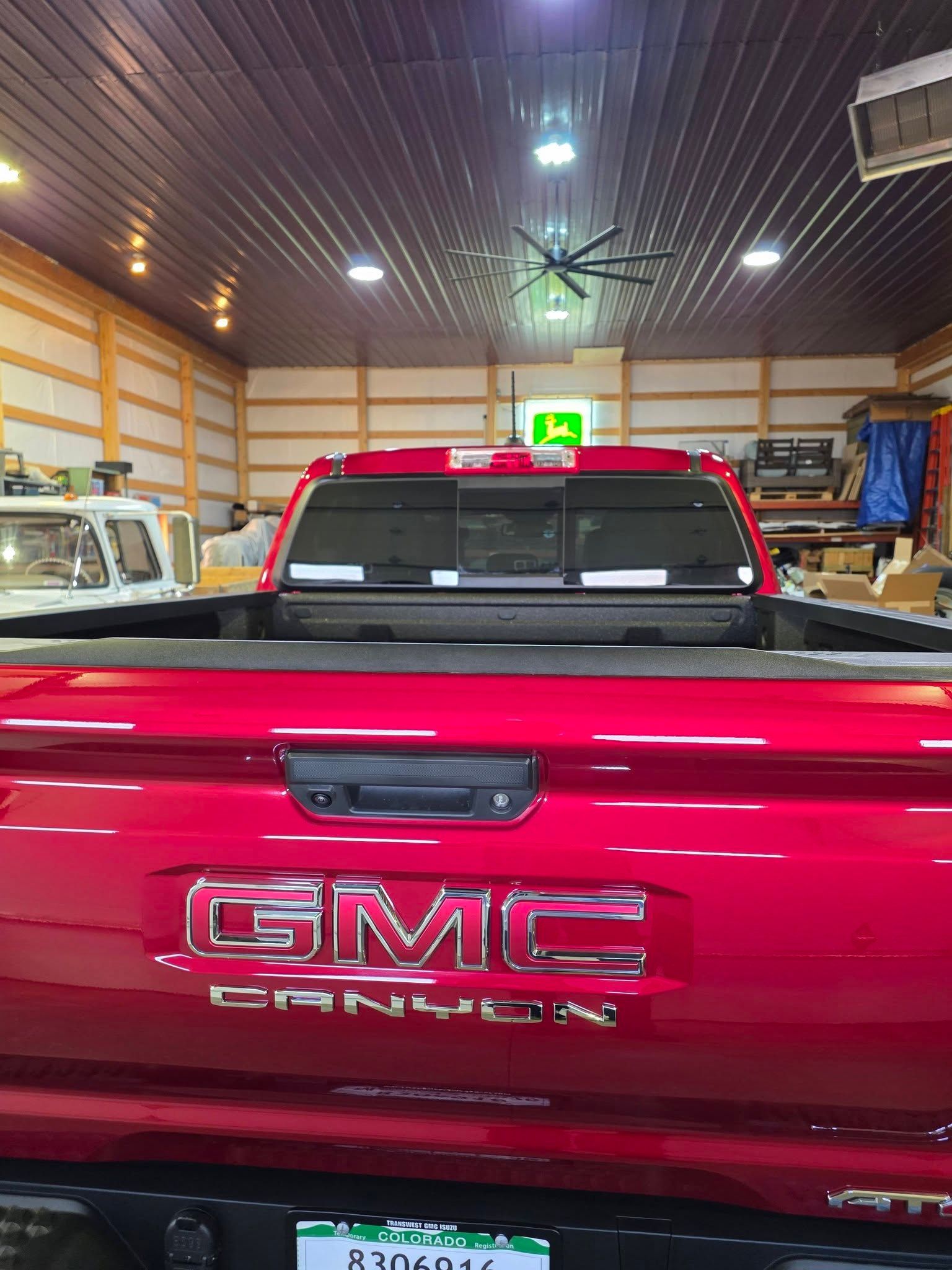 A rear view of a bright red GMC Canyon truck parked inside a bright workshop with a John Deere sign in the background.