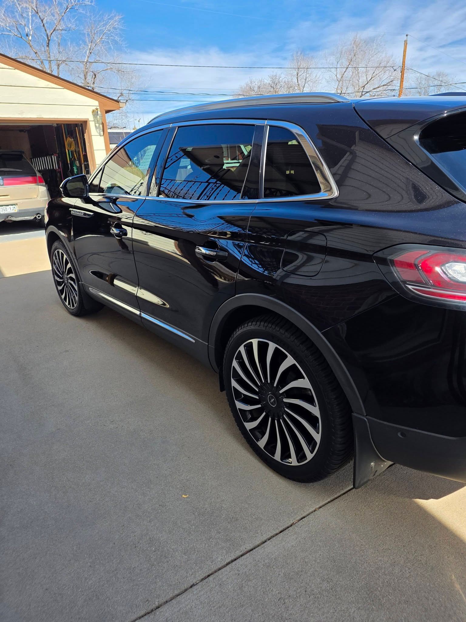 A shiny black SUV parked on a concrete driveway in front of a garage, featuring distinctive multi-spoke alloy wheels.