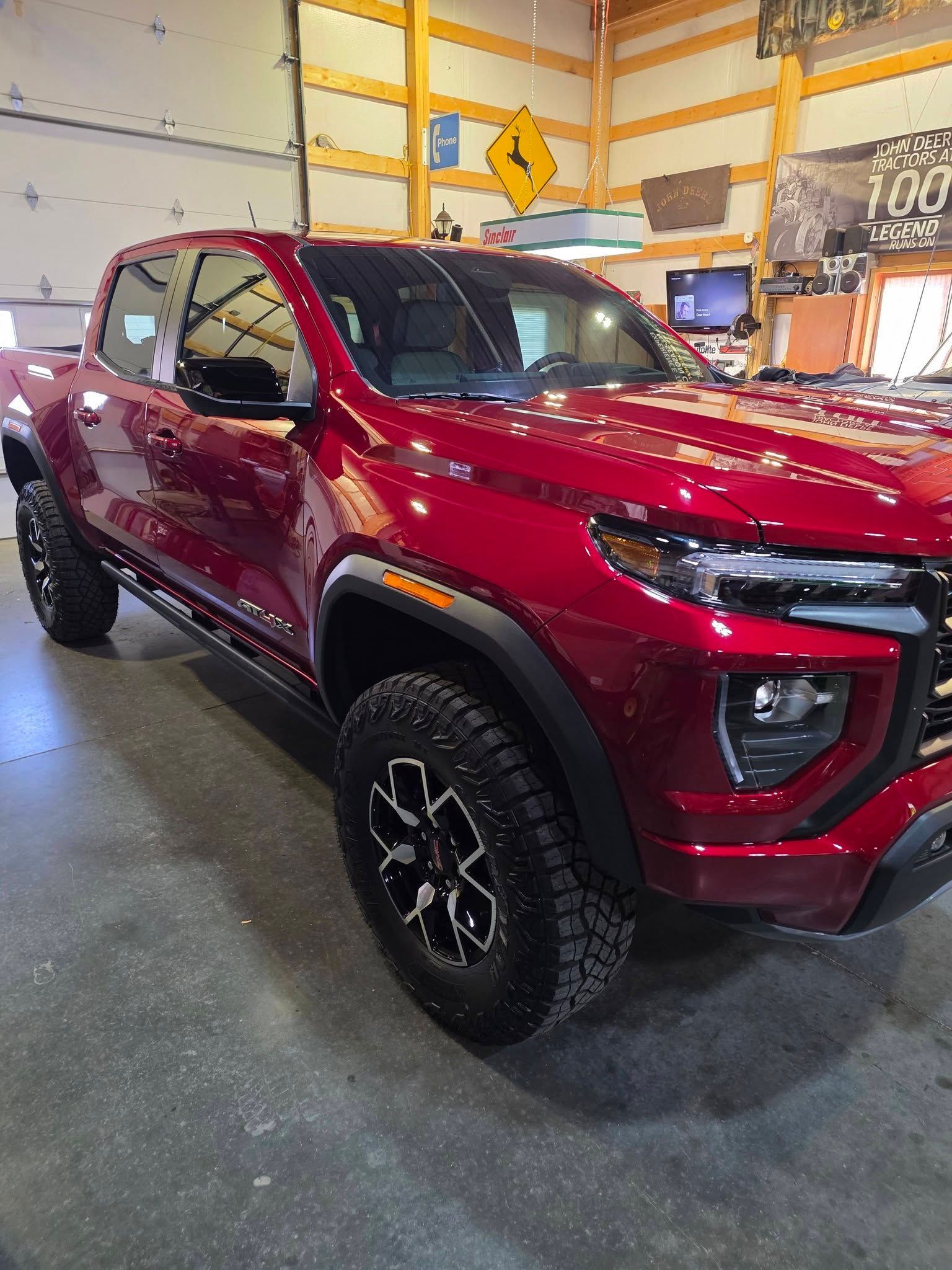 A metallic red Chevrolet Colorado pickup truck with off-road tires parked inside a garage.