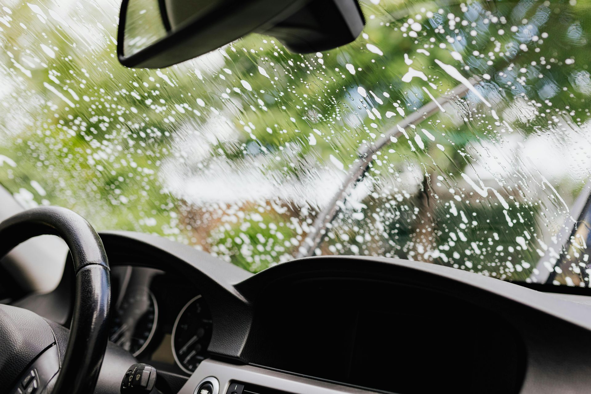 A view from inside a car looking out at a windshield covered in soap suds while being cleaned.