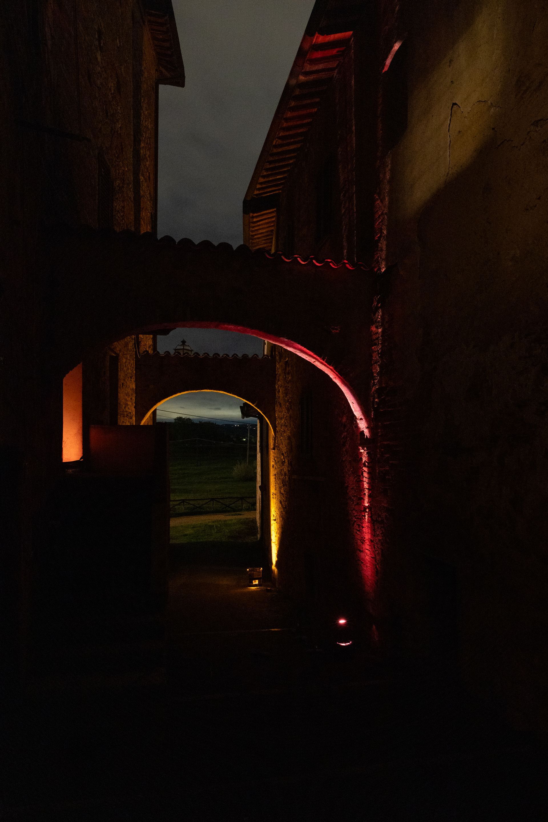 Dimly lit stone archway in Tuscany Italy, leading to an open field, showcasing the contrast between light and darkness.