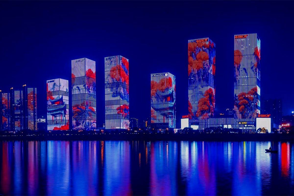 Skyscrapers lit by a vibrant media facade with red and blue digital projections, reflecting vividly 