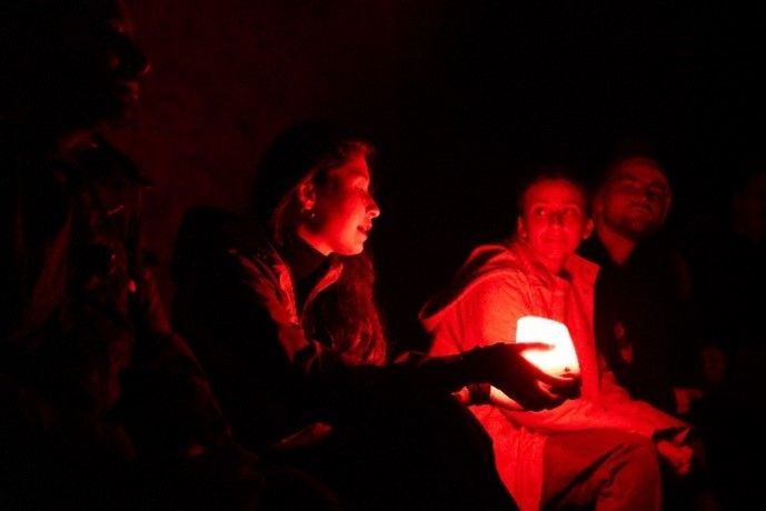 A small group of people gathered around a glowing light source in the dark, possibly sharing experiences or storytelling.