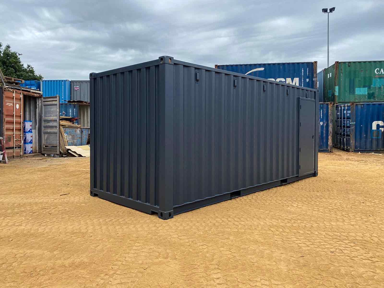 A black shipping container is sitting on top of a dirt field.