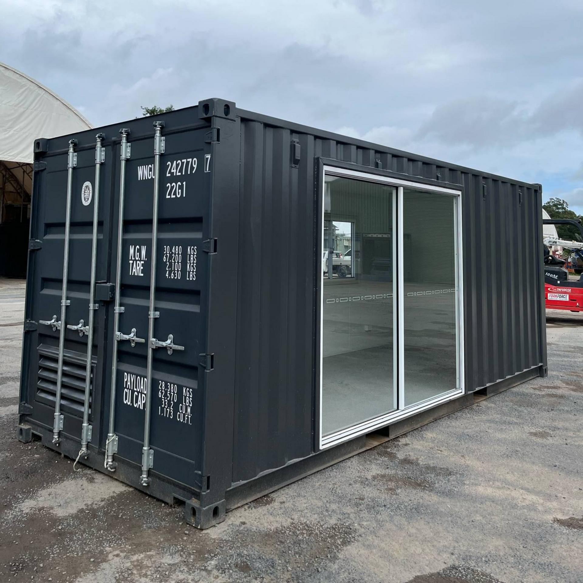 Black shipping container converted with sliding glass doors, outdoors on concrete, under cloudy sky — East Coast Containers Shipping Containers and Transport in Brisbane, QLD