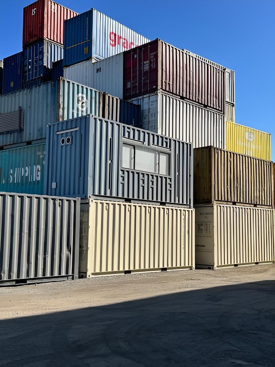 Stacked Shipping Containers in Various Colors Against a Clear Blue Sky — East Coast Containers Shipping Containers and Transport in Chevallum, QLD