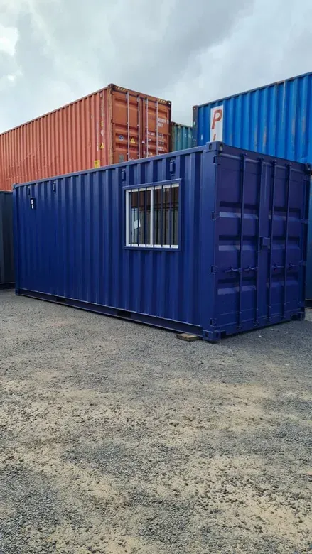 A blue shipping container with a window is sitting in a parking lot.