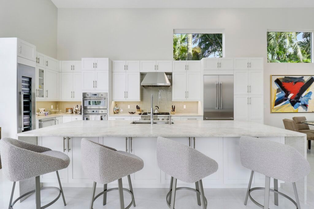 A kitchen with white cabinets and stools and a large island.