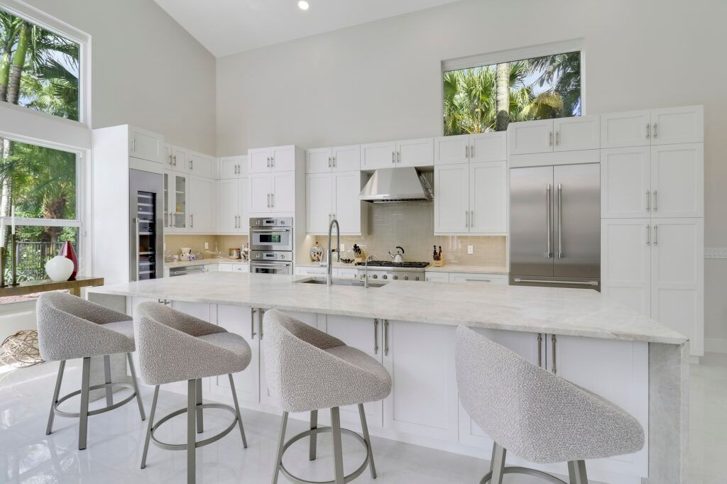 A kitchen with white cabinets and stools and a large island.