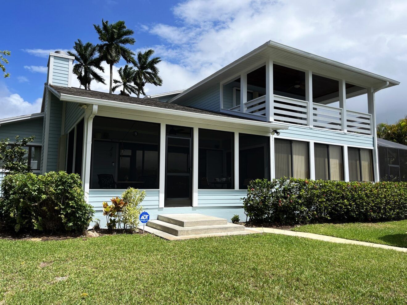 A large house with a screened in porch and palm trees in the background.