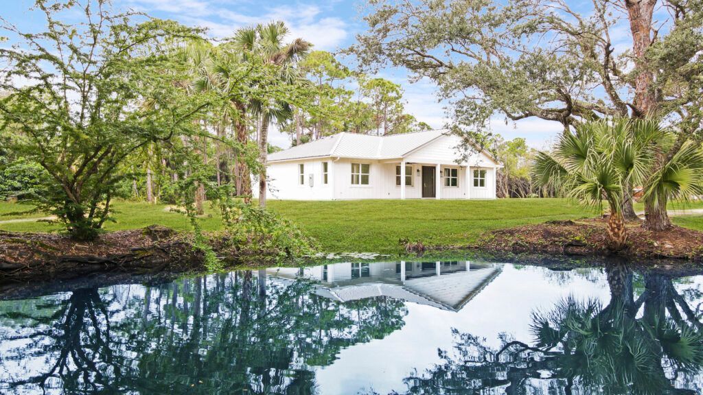 A white house is reflected in a pond surrounded by trees.