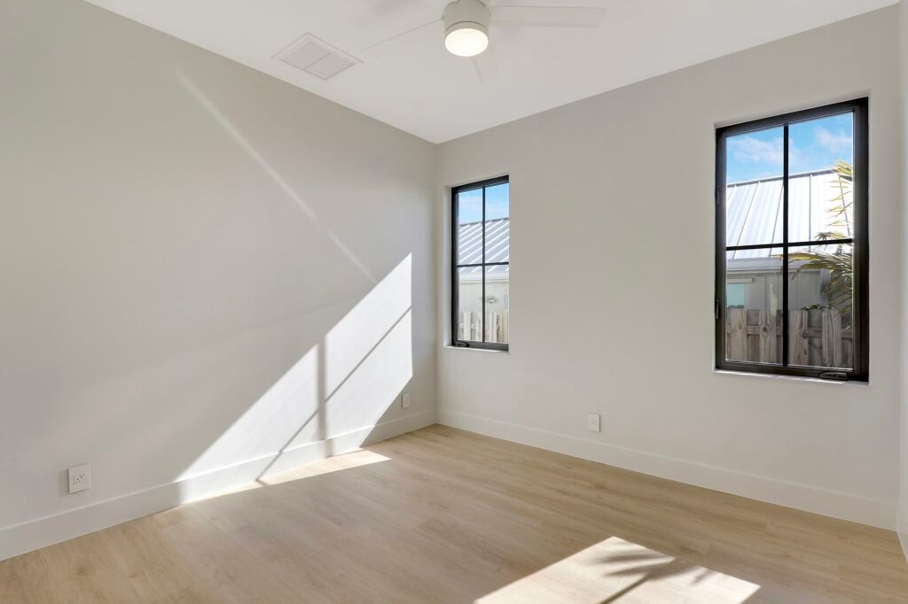 An empty bedroom with two windows and a ceiling fan.