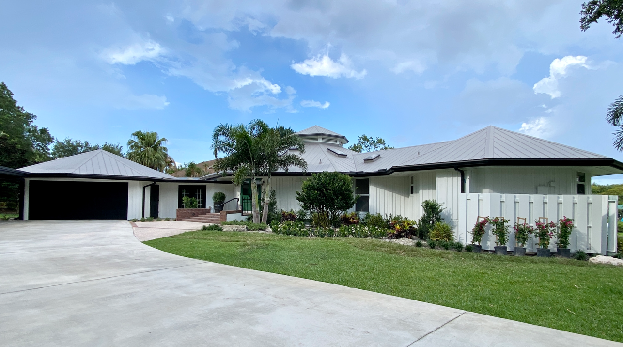 A large white house with a gray roof is sitting on top of a lush green field.