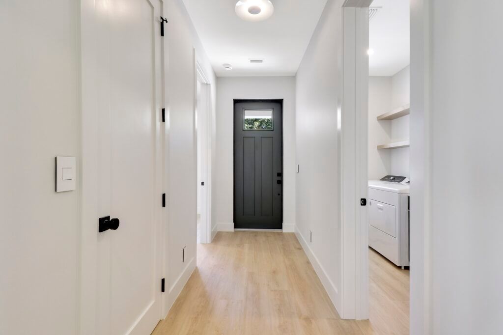 A hallway in a house with a black door and wooden floors.